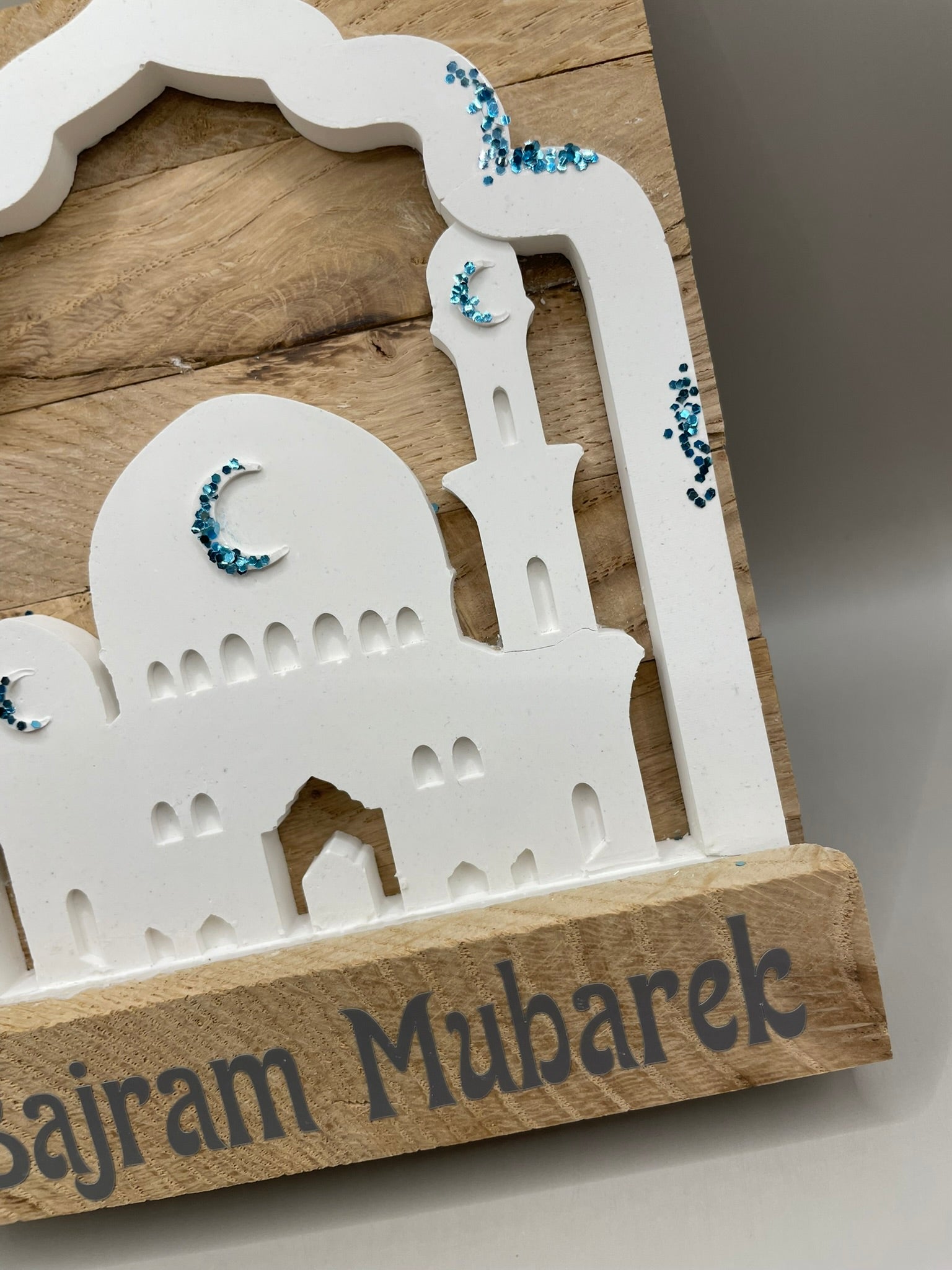 Geschenk in Form einer Mochee in weiß mit blauen Akzenten und der Überschrift "Bajram Mubarek" auf einem Holzgestellt